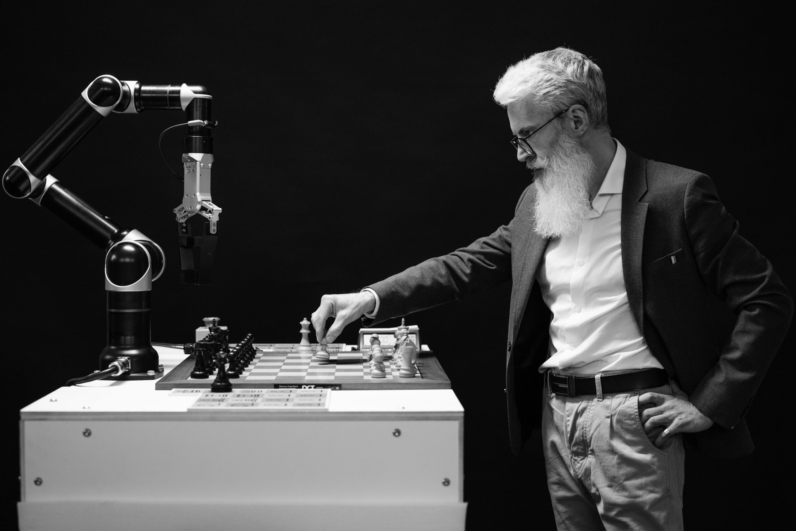 Homme mûr à barbes blanches jouant une partie d'échecs contre un bras robotisé industriel