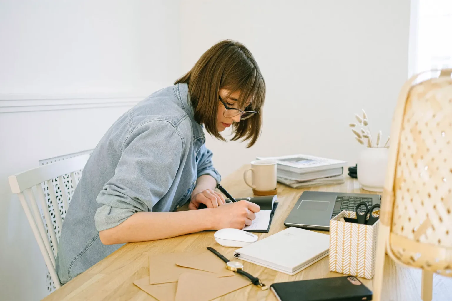 Une responsable marketing écrit dans un carnet à son bureau en bois, ordinateur portable ouvert à côté d'elle.